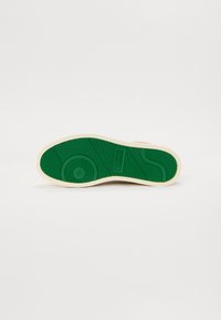 Talpa pantofului prezintă o suprafață texturată din cauciuc verde cu un model ondulat și detalii circulare, bordată de o margine de culoare crem.