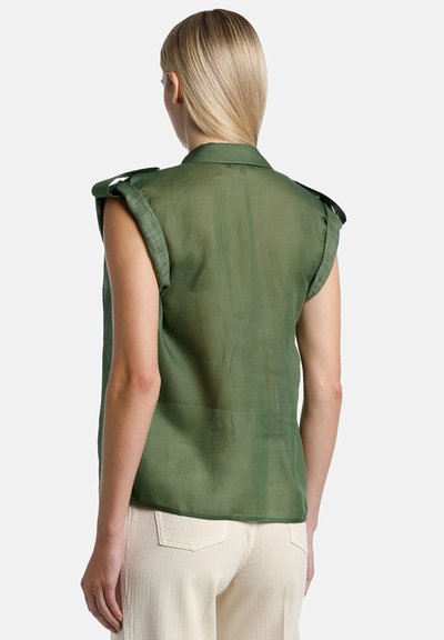 Green sleeveless shirt with a sheer texture, shoulder details, and a collared neckline, paired with cream-colored trousers.