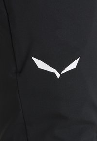 Svart treningsplagg laget av glatt stoff, med en hvit geometrisk logo på forsiden, med en tettsittende design og minimale sømdetaljer.