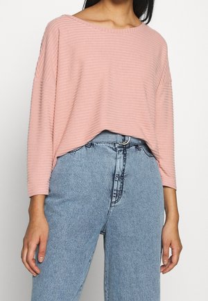 Maglione a coste di un rosa chiaro, con scollo ampio e maniche a tre quarti, abbinato a jeans in denim azzurro chiaro a vita alta.