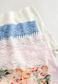 Sous-vêtements empilés avec des motifs floraux, rayés et unis, avec des bordures en dentelle crème, bleu, rose et motifs floraux sur fond clair.