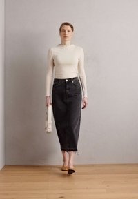 Schwarzer Jeansrock mit ausgefranstem Saum, kombiniert mit einem rippenförmigen, hellen Langarmoberteil mit Wellenkragen, getragen mit beigen Ballerinas.