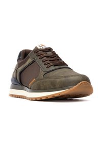 Zapatillas de deporte verde oliva con malla marrón y detalles de ante, que presentan costuras naranjas, cordones redondos y una suela de goma con un diseño de dibujo.