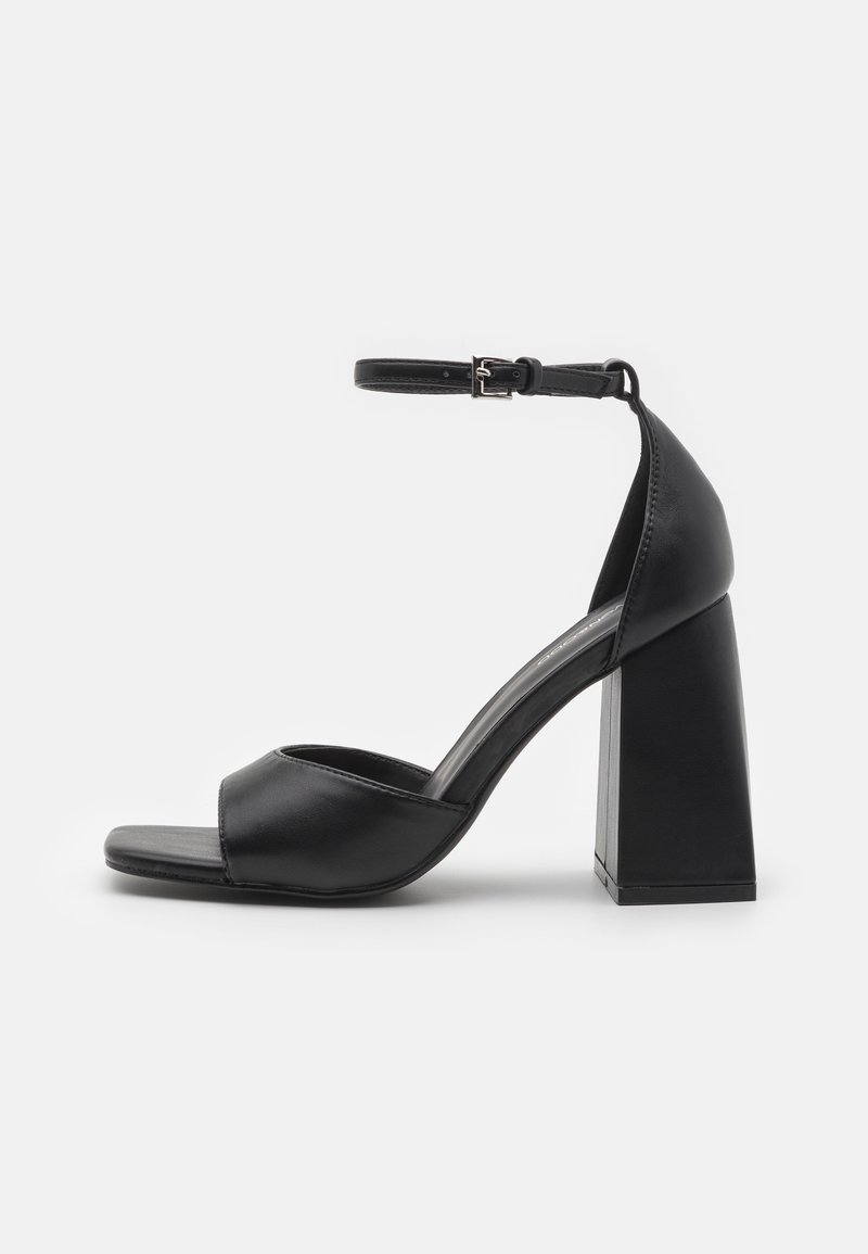 Des sandales à talons noirs présentent un dessus en cuir lisse, un bout ouvert, une sangle de cheville avec boucle et un large talon carré.