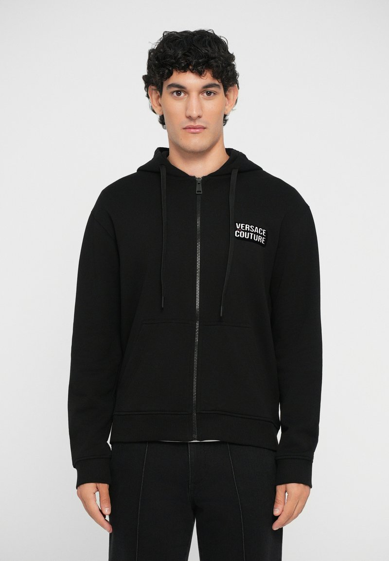 Mustmust värvi tõmbluku jack, mis on valmistatud puuvillast, esiPOOLKOTI ja joontega, ning millel on rinna peal "Versace Couture" logo.