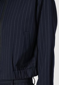 Navyblauwe jumpsuit met witte strepen; heeft een ritssluiting aan de voorkant, een elastische taille en zijzakken; gemaakt van een textuurstof.