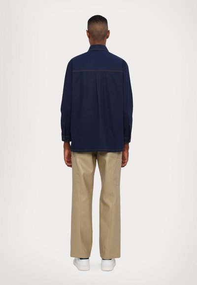 Camicia a maniche lunghe blu navy con colletto a punta, cuciture a contrasto e vestibilità rilassata, abbinata a pantaloni palazzo beige chiaro.