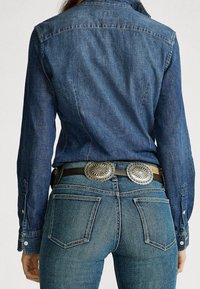 Jeansskjorta i mörkblått, med knäppta stängningar och krage, tillsammans med blå jeans och ett svart bälte med silverdetaljer och utsmyckade accenter.