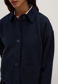 Navy blue wool jacket with a collar, front button closure, and two front pockets. Soft texture and relaxed fit with dropped shoulders.