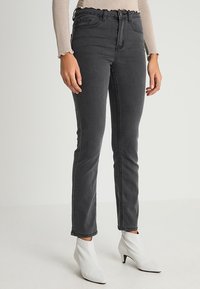 Jeans negros de cintura alta con un ajuste slim y cinco bolsillos, que cuentan con un zipper frontal y un sutil desgastado.