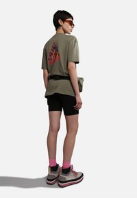 Camiseta Holgada de color verde oliva con un gráfico vibrante en la parte posterior, shorts negros, calcetines rosas y botas gruesas grises con acentos rosas.