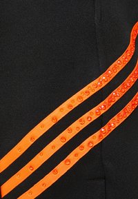 Svarta joggers i tyg med tre orange randiga detaljer, prydda med runda, glänsande paljetter längs kanterna.