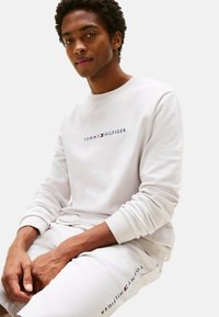 Felpa e pantaloni in cotone bianco con logo "TOMMY HILFIGER" in blu navy e rosso. Polsini a costine sulla felpa e sui pantaloni.