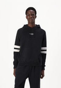 Čierna mikina s kapucňou, predným vreckom, nastaviteľnou kapucňou s šnúrkou a bielymi prúžkami na rukávoch. Logo umiestnené na hrudi.