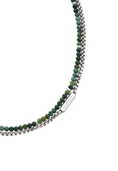 Bracelet en pierres vertes composé de perles, avec une chaîne en métal argenté et un fermoir rectangulaire en argent gravé de texte. Texture lisse et brillante.