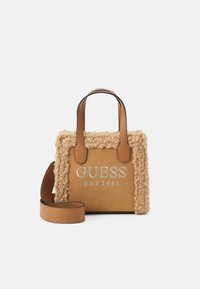 Tan handtas met een gestructureerde schapenwolachtige buitenkant, leren accenten en een zilver geborduurd logo. Voorzien van korte handvatten en een afneembare schouderband.