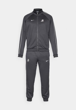 Dunkelgrauer Nike Trainingsanzug mit Reißverschlussjacke und Jogginghosen, versehen mit weißen Paspeln und Los Angeles Lakers-Logos auf der Brust und dem Oberschenkel.