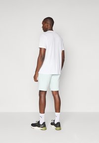 T-shirt branca de mangas curtas, calções mint claros, sapatilhas pretas de desporto com detalhes verdes, meias brancas. Design simples, sem padrões.