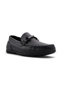Zapatos negros de piel de tipo slip-on con un acabado texturizado, detalles de costura y un acento decorativo de metal negro en el lateral. Suela de goma de perfil bajo.