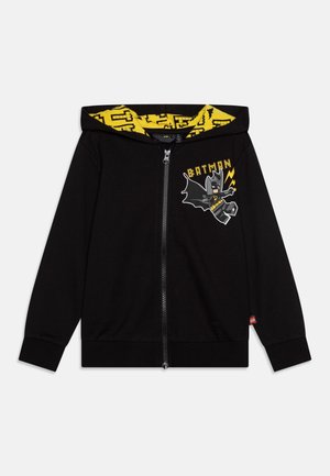 Sweat à capuche noir zippé avec un motif de figurine Batman LEGO jaune sur la poitrine et une doublure de capuche à motif jaune avec un design de briques LEGO.