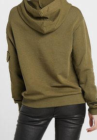 Sudadera con capucha color verde oliva que presenta una capucha forrada, mangas largas y puños acanalados. La tela es suave con una textura lisa y un ajuste relajado.