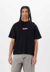 Black cotton t-shirt with short sleeves and a relaxed fit. Features pink text "Cultivate Growth" at the chest. Pair with light gray shorts.
