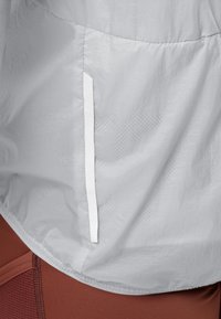 Lichte, grijze sportjacket met een gestructureerde afwerking; voorzien van een witte zijzak en een strakke, minimalistische uitstraling.