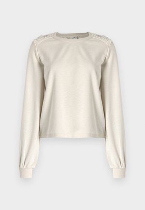 Svijetlosmeđi krojeni dukserica s dugim rukavima, uskim manžetama i dekorativnim perlicama na ramenima. Glatka tekstura tkanine.