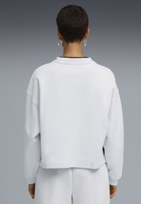 Sudadera de algodón blanca con un corte relajado, hombros caídos y cuello acanalado. Diseño minimalista sin patrones ni herrajes visibles.