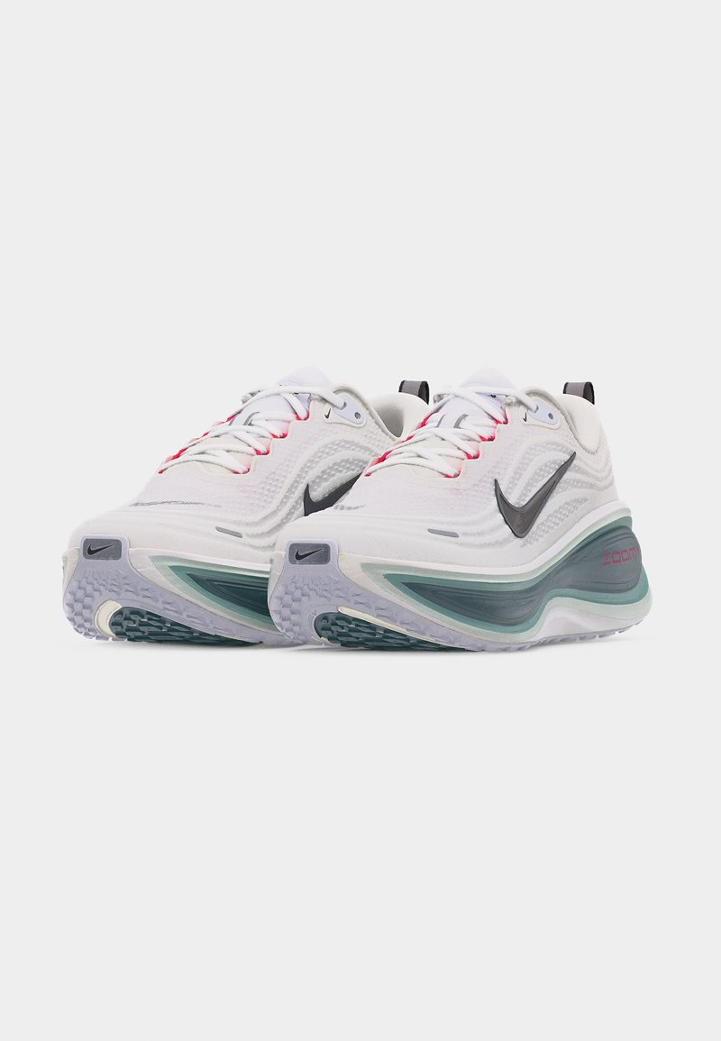 Para białych sportowych tenisówek z czarnym logo Nike w kształcie znaku Swoosh, zielonymi i fioletowymi akcentami oraz widoczną amortyzacją Zoom Air na jednolitym tle.