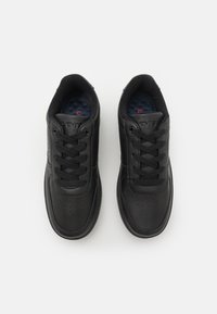 Baskets en cuir noir avec un bout arrondi. Elles présentent des perforations sur le dessus, des lacets noirs et une semelle intérieure texturée bleue.