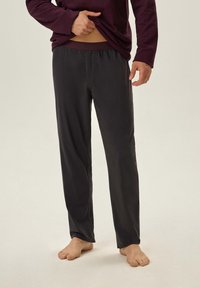 Ciemnoszare spodnie dresowe z elastycznym pasem, wykonane z miękkiego materiału. Prosty krój, lekka konstrukcja. Noszone na boso z długim rękawem.