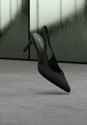 Μαύρο γυναικείο παπούτσι με ψηλό τακούνι και λουράκι στον αστράγαλο, με μύτη, με εμπορικό σήμα «ANNA FIELD», αιωρούμενο ελαφρώς πάνω από γκρι επιφάνεια.