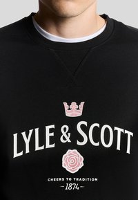 Felpa nera con collo a costine, grande scritta bianca "LYLE & SCOTT", una corona rosa e una grafica di una rosa rosa. Vestibilità casual.