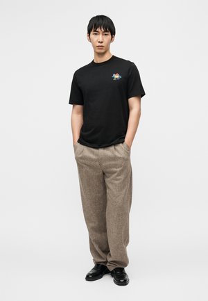 Sort bomuld t-shirt med et farverigt motiv på brystet, kombineret med løstsiddende beige teksturerede bukser og sorte sko.