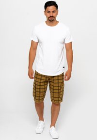 Vit T-shirt med rund hals, kombinerad med bruna rutig cargoshorts med fickor och vita sneakers. Tyget verkar lätt och avslappnat.