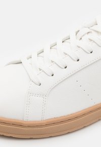 Białe skórzane sneakersy z płaskimi bawełnianymi sznurówkami, gumową podeszwą i subtelnymi perforacjami po bokach dla wentylacji. Gładka tekstura i klasyczny design.