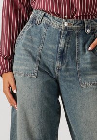 Hoge taille spijkerbroek in lichtblauw met een gestructureerde afwerking, voorzien van voorste plooien, zijzakken en metalen knopen.