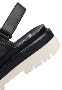 Sandale en cuir noir avec une semelle épaisse blanche à relief et une bride Velcro ajustable au talon.