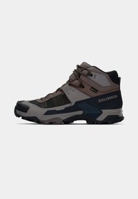 Shoe de caminhadas de cano médio com um design em cinza e azul escuro, material sintético, biqueira reforçada, parte superior texturizada e sistema de atacadores para suporte.