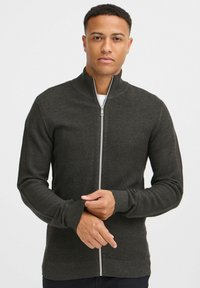 Veste à fermeture éclair gris foncé en tissu texturé, coupe slim, col montant et poignets côtelés. Dotée d'une fermeture éclair argentée et d'un motif tricoté subtil.