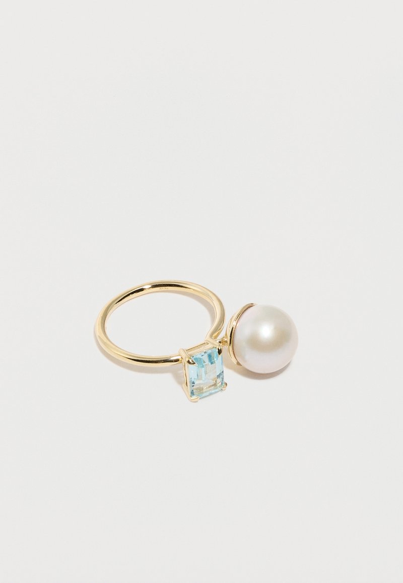 Bague ouverte en or présentant une grande perle blanche à une extrémité et une pierre précieuse bleu clair taillée en carré à l'autre, sur un fond blanc.