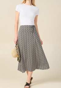 Falda midi con estampado floral en negro y crema, con cintura ajustable, combinada con una camiseta blanca ajustada y sandalias negras con tiras. Bolso de paja trenzada.