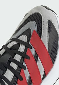 Čierne, šedé a červené tenisky majú zvršok z sieťoviny a semišu, čierne šnúrky a tri červené prúžky, zaoblenú špičku a bielu podrážku.