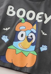 Graues T-Shirt mit einer Cartoon-Hund mit blau-orangefarbenem Design, der ein Kürbiskostüm trägt, und dem Wort "BOOEY" in Weiß darüber.
