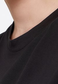 Sort bomulds t-shirt med rund hals og korte ærmer, der fremhæver en glat tekstur og syningsdetaljer langs kraven.
