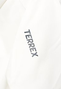 Gros plan d'un tissu blanc avec le texte gras noir « TERREX » imprimé en diagonale sur la surface.