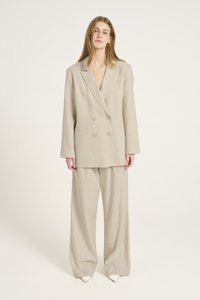 Beige dubbelgevoerde blazer met grote knopen en wijde broekspijpen. Lichtgewicht stof met een gladde textuur en een ontspannen pasvorm. Puntige witte schoenen.