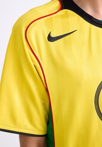 Yellow sports jersey made of lightweight fabric, featuring a black Nike logo, red accents along the seams, and a rounded collar.