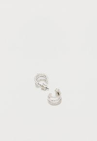 Μικρά ασημένια σκουλαρίκια κρίκοι με ενσωματωμένα διαυγή πολύτιμους λίθους και κούμπωμα με καρφί, τοποθετημένα πάνω σε λευκή απλή επιφάνεια.